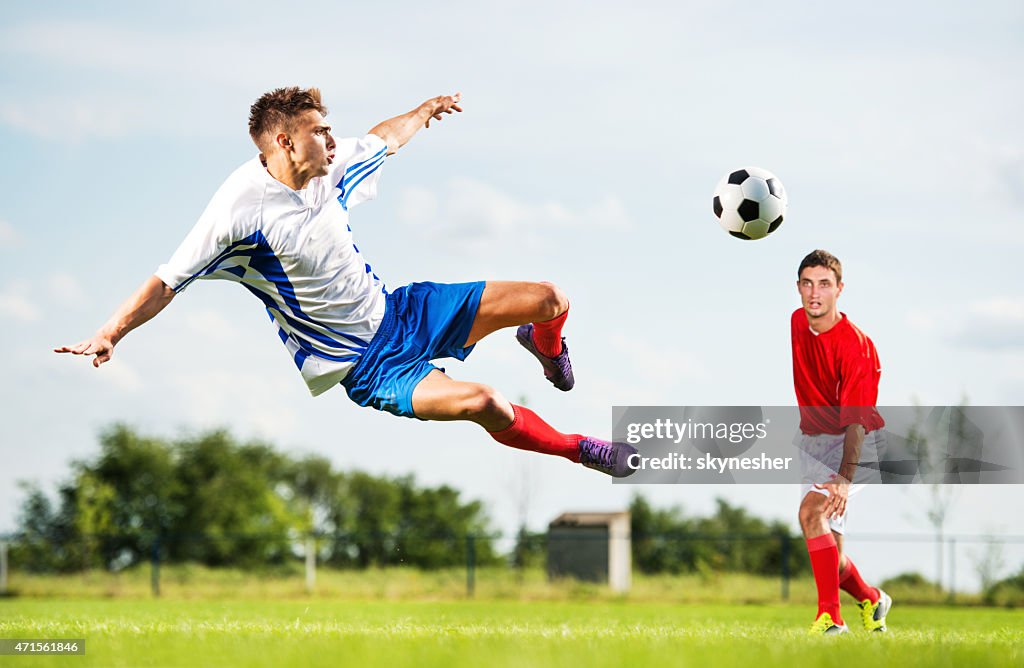 Jogador de futebol chutando a bola enquanto está no ar.