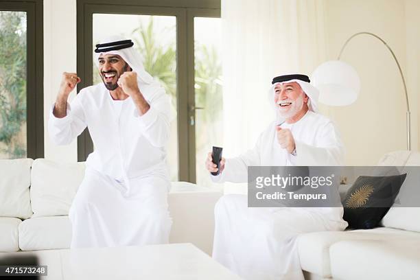 middle eastern father and watching soccer on tv at home. - emirati enjoy stock pictures, royalty-free photos & images