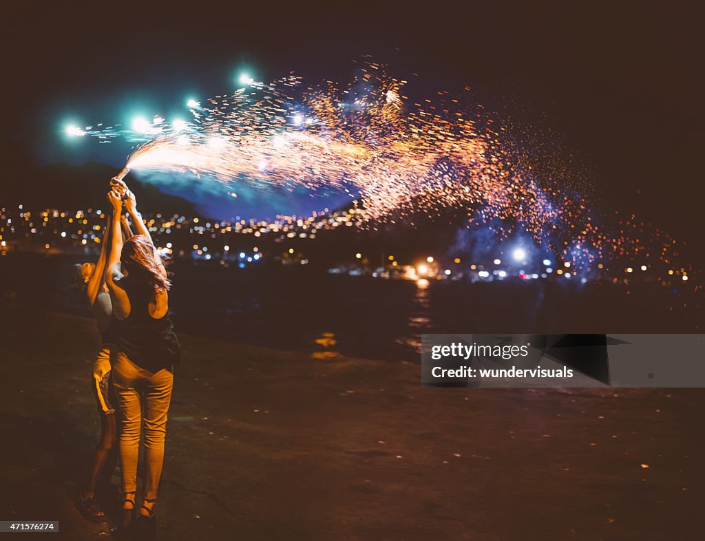 Teen girls holding sparkling fireworks at night at the harbour