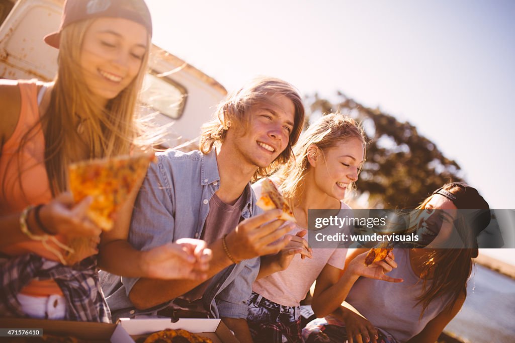 Teenaged friends sitting together outside eating pizza