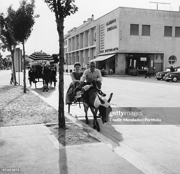 Man and a woman travelling on a donkey-drawn carriage. Cattolica, 1950s "