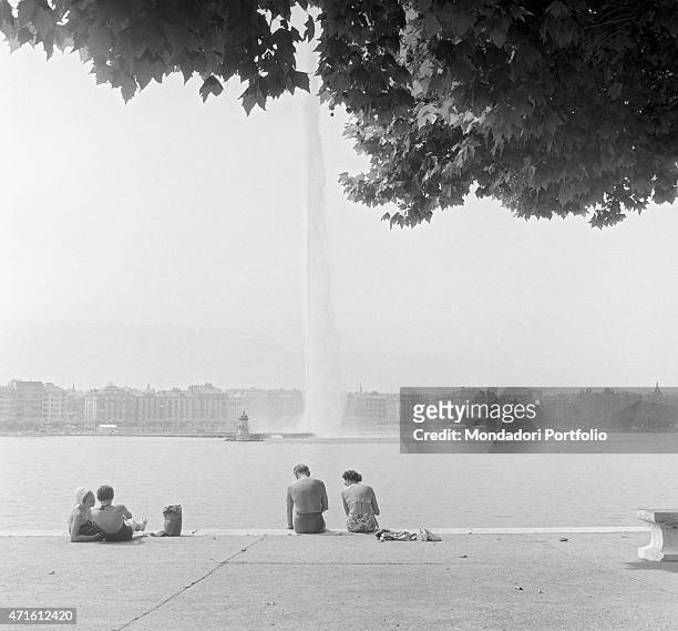 "Some people in swimsuit sunbathing by the lake in front of the Jet d'Eau. The city houses the Geneva Summit discussing issues about security, German...