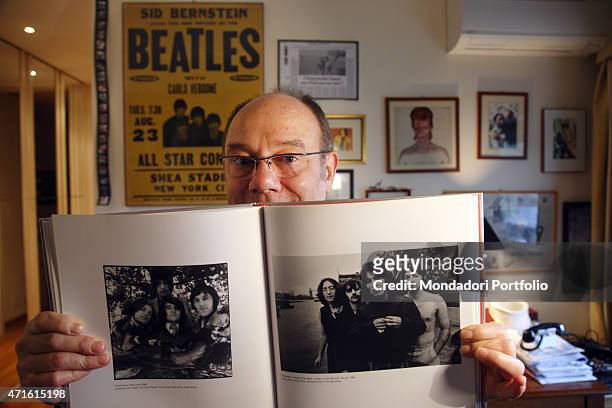 "The director and actor Carlo Verdone showing a picture from the catalogue Beatles to Bowie for a photo shooting at home. On the wall behind him, the...