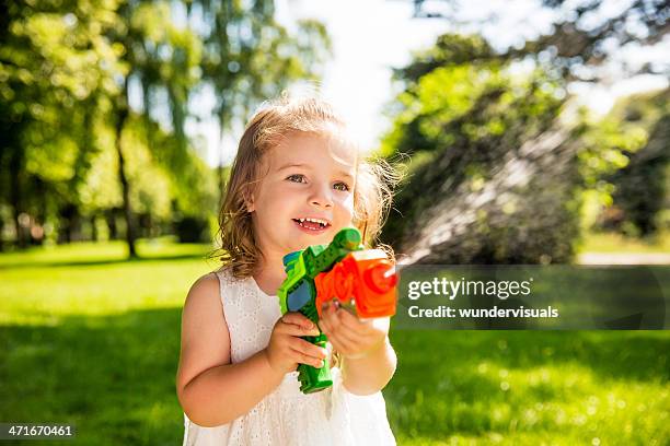 chica sonriente salpicaduras de agua con una pistola de agua - pistola de agua fotografías e imágenes de stock