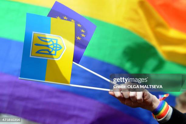 Protester holds the flags of Ukraine, bearing the country's coat of arms, and the European Union in front of a rainbow flag, as members and...