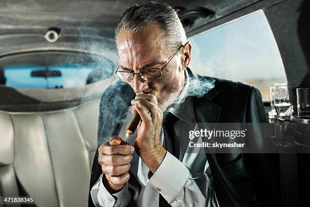mature adult businessman lighting up a cigar in limousine. - premium lighter stock pictures, royalty-free photos & images