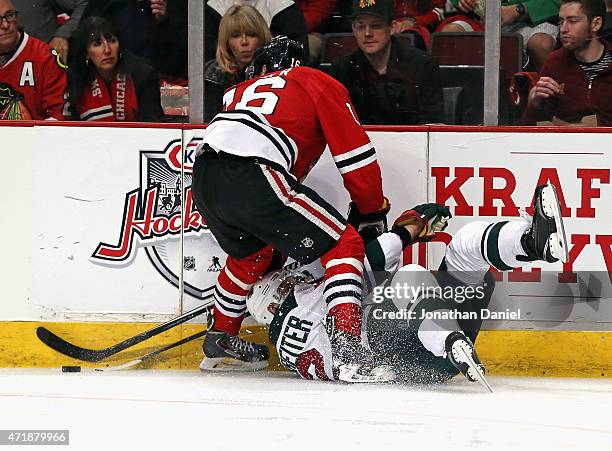Nino Niederreiter of the Minnesota Wild hits the ice as he battles for the puck with Marcus Kruger of the Chicago Blackhawks in Game One of the...