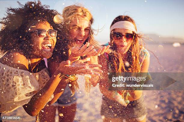 girls blowing confetti from their hands on a beach - summer beach girl party stockfoto's en -beelden