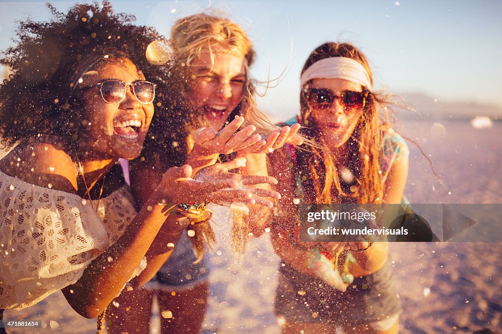 Girls blowing confetti from their hands on a beach