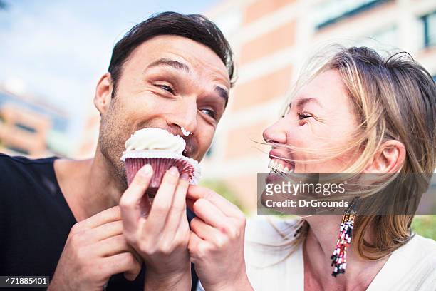 alegre pareja comiendo magdalenas con glaseado al aire libre - cupcake fotografías e imágenes de stock