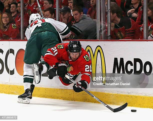 Brandon Saad of the Chicago Blackhawks is sent into air by Kyle Brodziak of the Minnesota Wild as he tries to get to the puck in Game One of the...