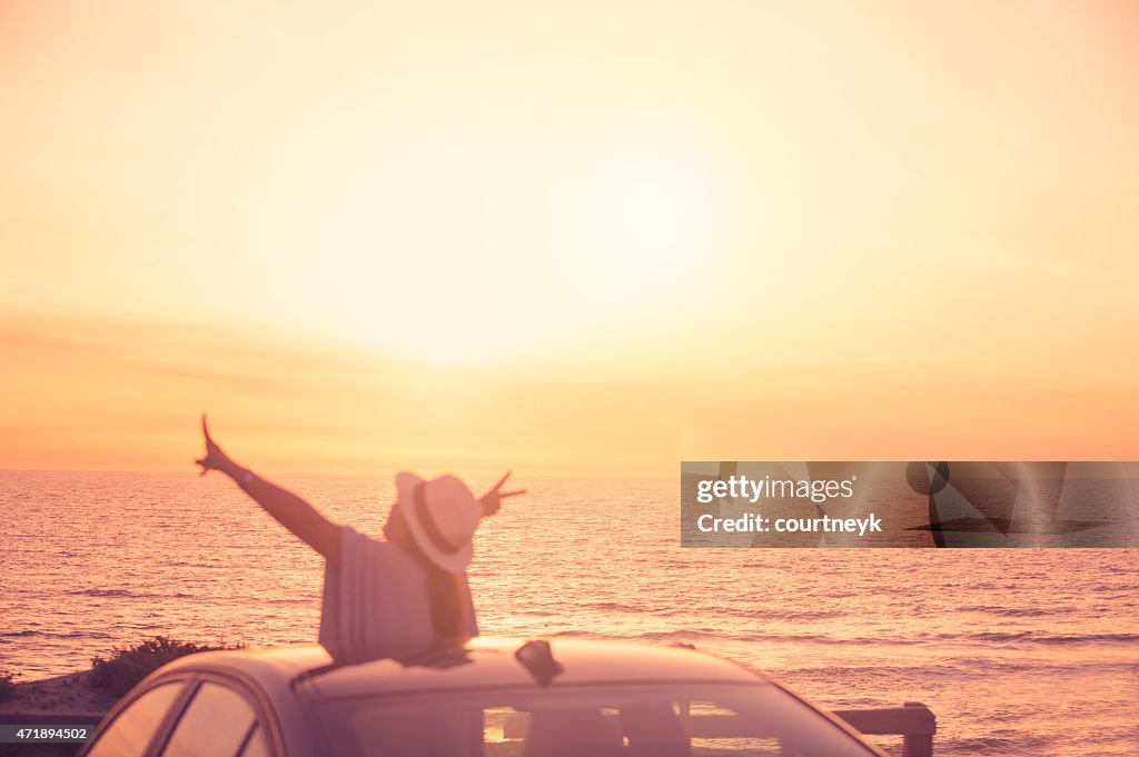 Mature woman leaning out of sunroof at sunset.