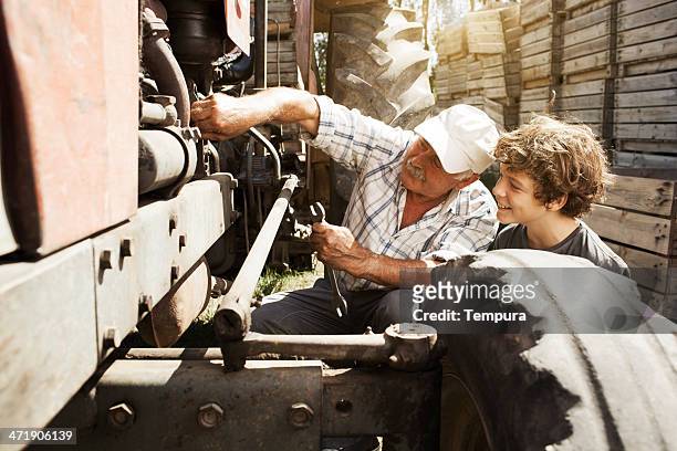 grandfather teaching grand son how to fix tractor. - tractor repair stock pictures, royalty-free photos & images