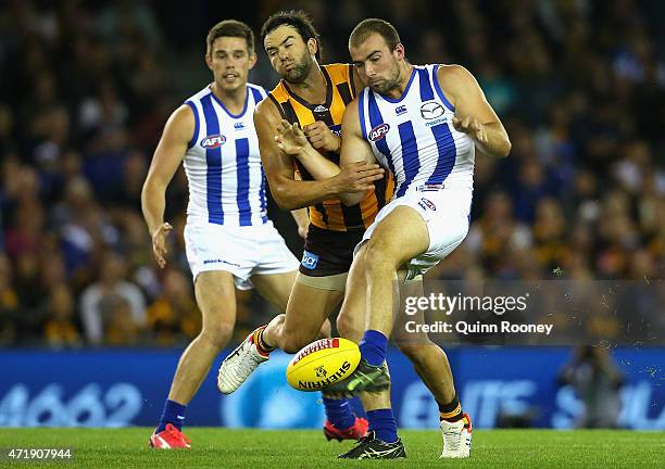 Ben Cunnington of the Kangaroos kicks whislt being bumped by Jordan Lewis of the Hawks during the round five AFL match between the North Melbourne...