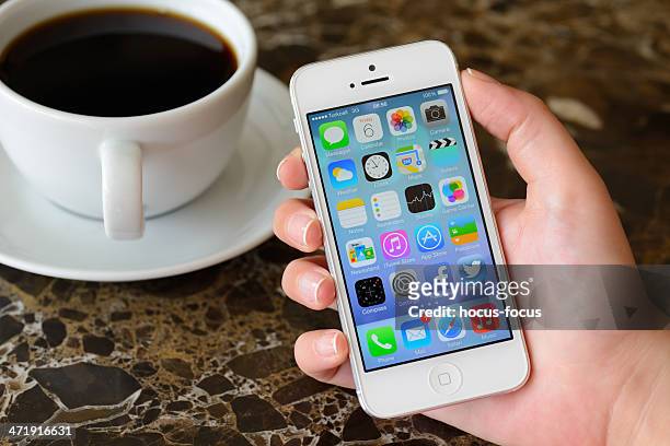 hand holding apple iphone 5 displaying home screen - holding iphone stockfoto's en -beelden