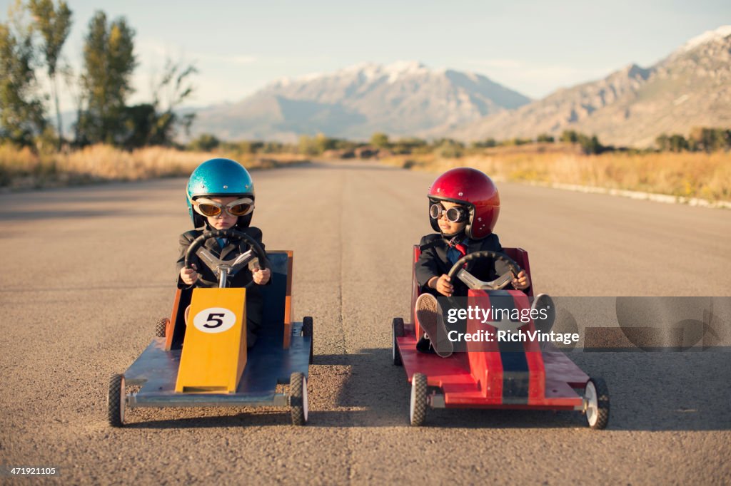 Two Business Boys Sit in Toy Cars on Street