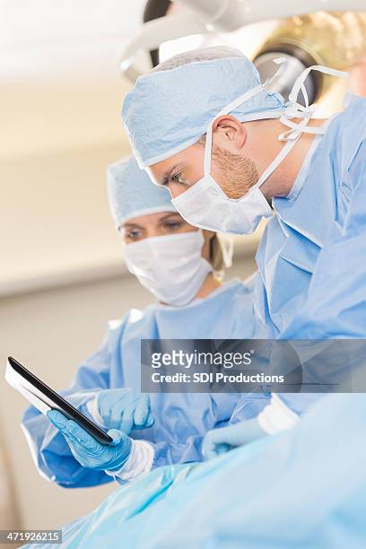 surgeon using digital tablet during surgical procedure in hospital - operating gown stock pictures, royalty-free photos & images