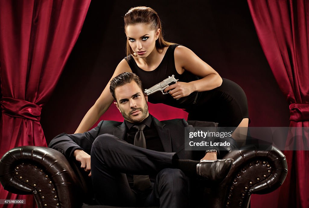 Woman pointing gun to man sitting on chair