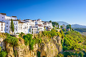 Houses on a cliff in Ronda, Spain surrounded by green trees