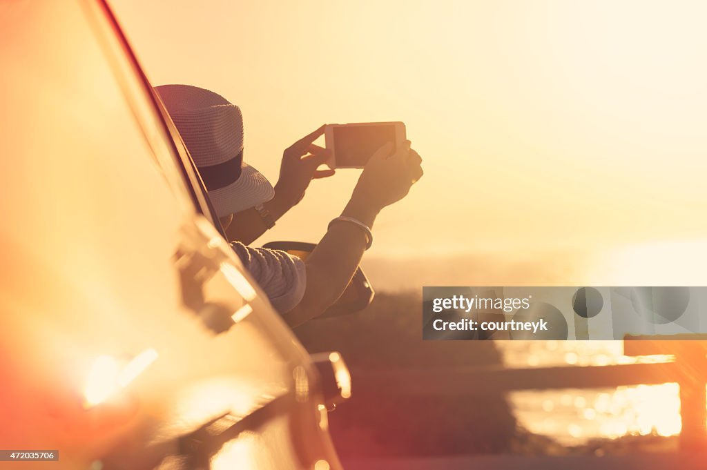 Woman taking a sunset photo in a car.