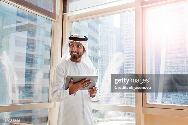 arab businessman using digital tablet in dubai office. - united arab emirates business stock pictures, royalty-free photos & images