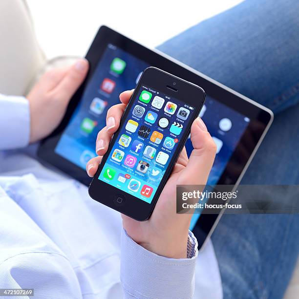 hands holding iphone 5 & apple ipad displaying ios 7 screen - ios greece stock pictures, royalty-free photos & images