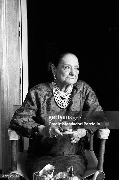 "American magnate Helena Rubinstein, portrayed in a moment of relaxation, sits with a cup of fine porcelain in hand and looks at her left;...