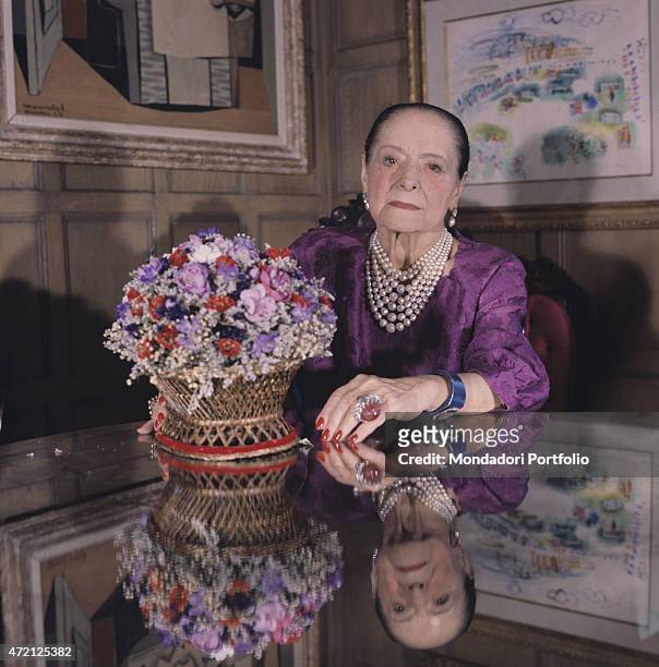 "Intense portrait of Helena Rubinstein, seated on a chair with a china cup in hand; the famous Polish born American entrepreneur of cosmetics...