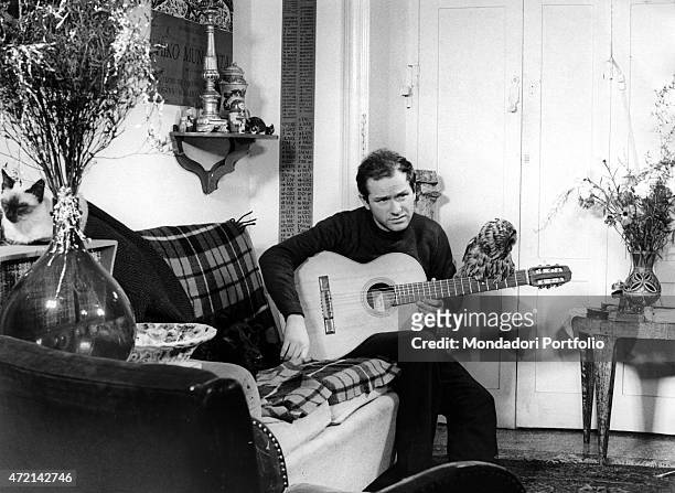 Italian singer-songwriter Gino Paoli sitting on a sofa with an owl perched on the guitar. 1960s