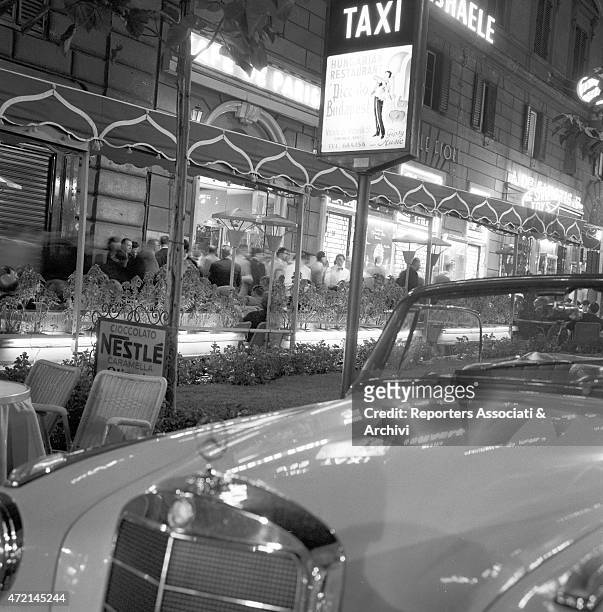 View of the pavement on via Veneto with the tables of the well-known 'Cafè de Paris' and the 'Taxi' sign and detail of a Mercedes car in the...