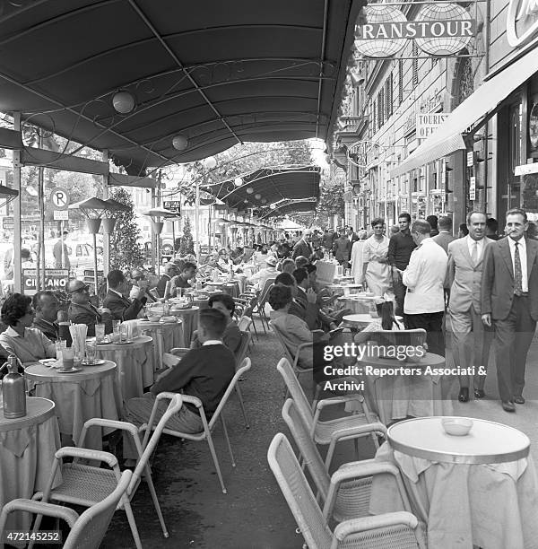 View of the pavement on via Veneto with people sitting at the tables of a café and people walking. Rome, 1958