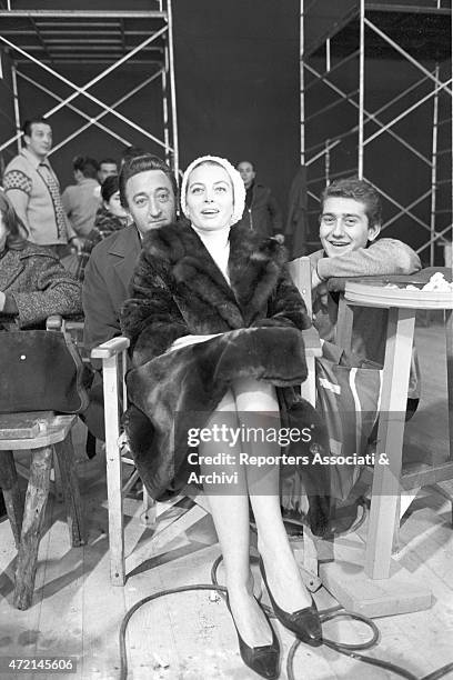 French actress Capucine amused smiling next to two men in the backstage of the film 'The Pink Panther'. Cortina d'Ampezzo, 1963