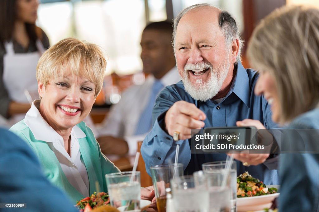 Senior man and woman laugh with friends over meal