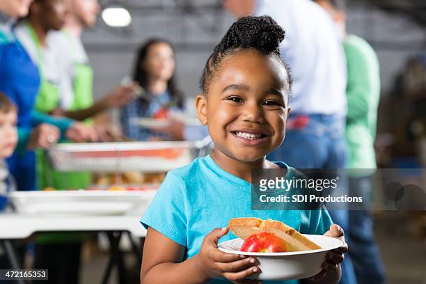 little girl holding bowl at soup kitchen or food bank - food staple stock pictures, royalty-free photos & images