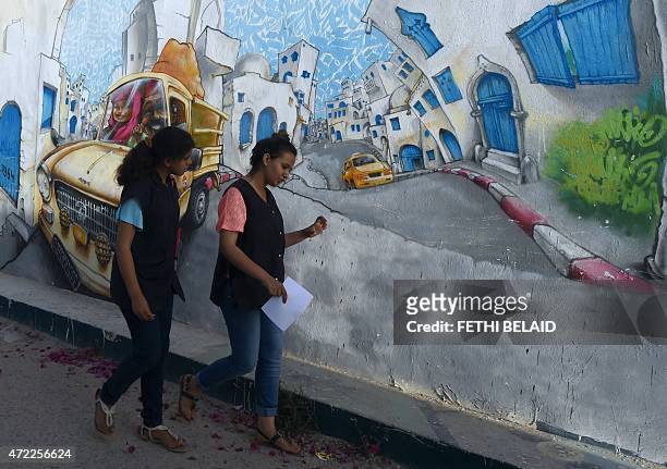 Tunisian girls walk passed a wall covered in graffiti near the Ghriba Synagogue on May 5, 2015 on the eve of the annual Jewish pilgrimage to the...