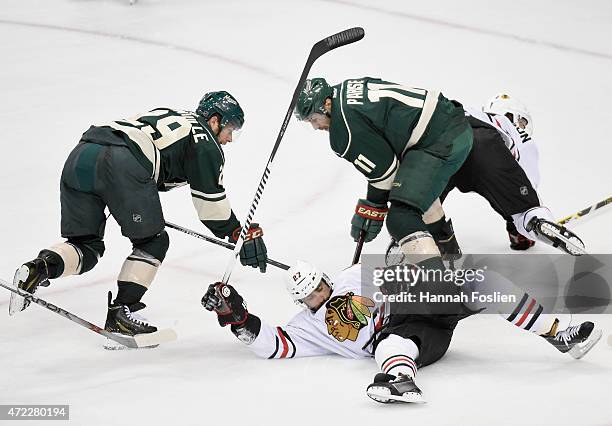 Johnny Oduya of the Chicago Blackhawks falls onto the puck as Jason Pominville and Zach Parise of the Minnesota Wild attempt to get the puck during...