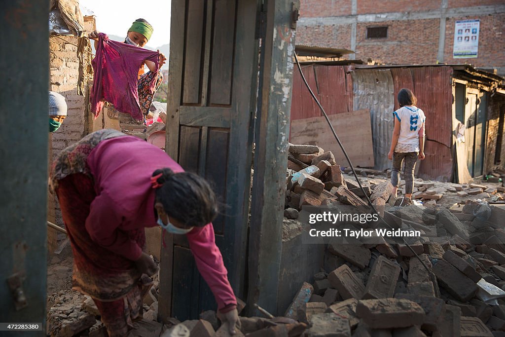 Nepali residents clear rubble and collect items from their...