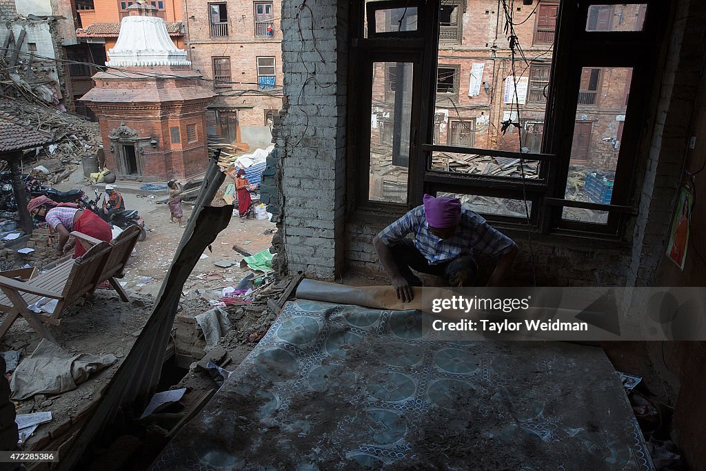 Nepali residents clear rubble and collect items from their...