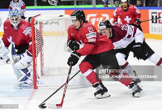 Goalkeeper Reto Berra of Switzerland observes as his teammate forward Kevin Fiala and forward Andris Dzerins of Latvia vie for the puck during the...