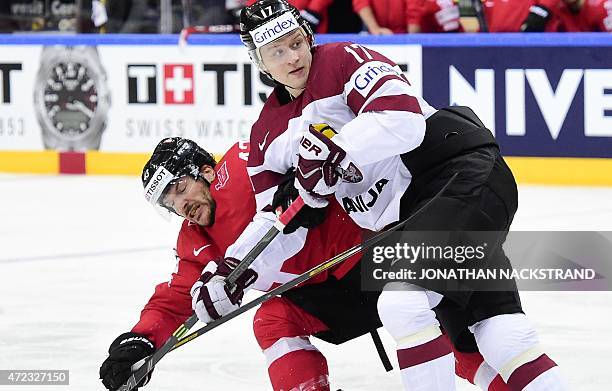 Forward Morris Trachsler of Switzerland and forward Kaspars Saulietis of Latvia vie for the puck during the group A preliminary round match...