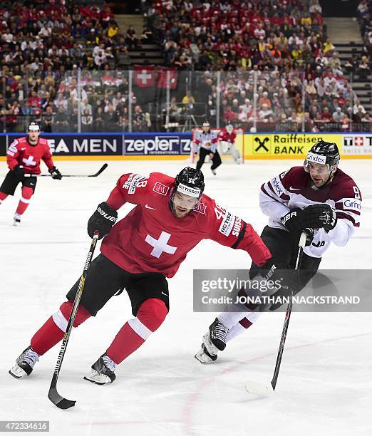 Defender Krisjanis Redlihs of Latvia and forward Matthias Bieber of Switzerland vie for the puck during the group A preliminary round match...