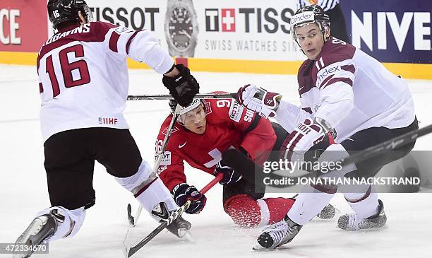 Forward Kaspars Daugavins and defender Kristaps Sotnieks of Latvia vie for the puck with forward Damien Brunner of Switzerland during the group A...