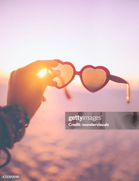 heart-shaped sunglasses being held with a sunset behind - heart sunglasses stock pictures, royalty-free photos & images