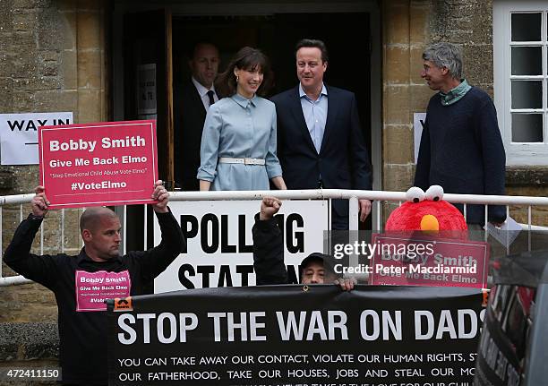 Prime Minister David Cameron and his wife Samantha look at demonstrators as they leave a polling station after casting their vote in the general...