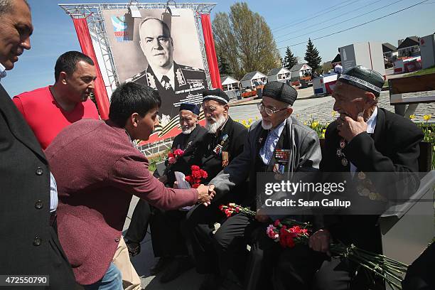Passer-by greets Uzbek World War II veterans of the Soviet Red Army sitting near a portrait of World War II Russian General Georgy Zhukov, who led...