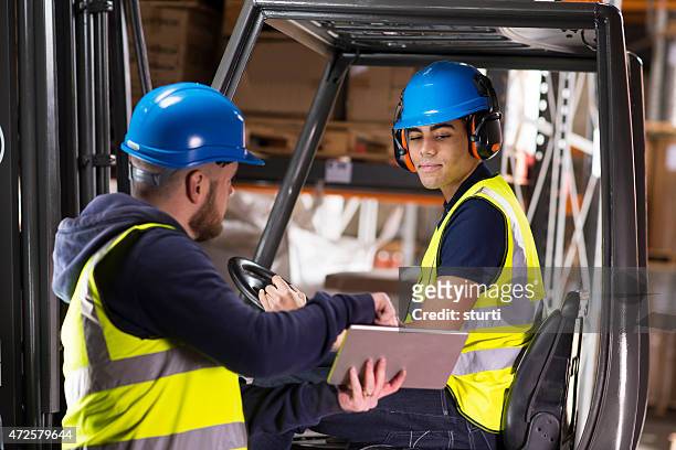 warehouse supervisor chats to young forklift truck driver trainee - forklift stock pictures, royalty-free photos & images