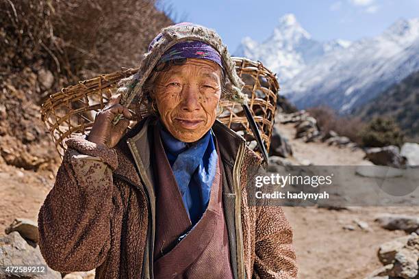 old woman carrying basket in himalayas - sherpa village stock pictures, royalty-free photos & images