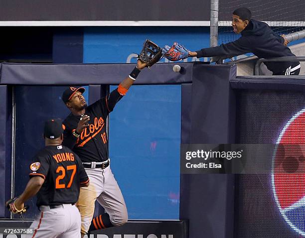 Adam Jones of the Baltimore Orioles tries to make a catch on a hit by Alex Rodriguez of the New York Yankees as a fan also goes for the ball in the...