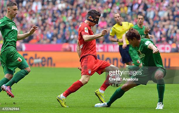 Robert Lewandowski of Bayern Munich wearing a mask and Dominik Kohr and Jeong-Ho Hong of Augsburg fight for the ball during the Bundesliga soccer...