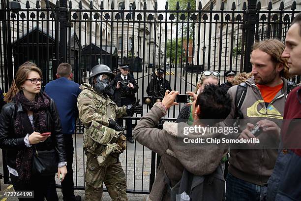 Man in military fatigues, a gas mask and a helmet with anarchy symbols poses for a photograph outside the security fence protecting Downing Street...